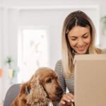A woman with a dog opening a box of gifts showing Dog Gift Subscription Boxes
