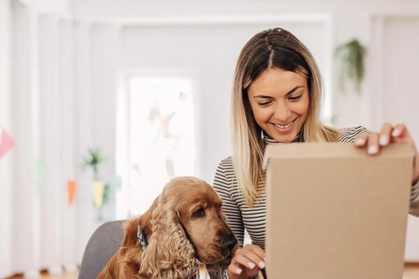 A woman with a dog opening a box of gifts showing Dog Gift Subscription Boxes